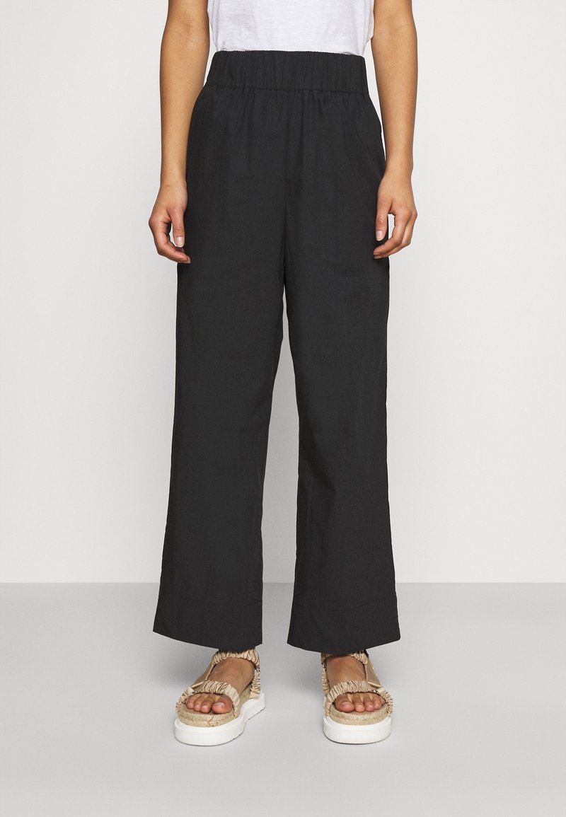 Pantalons larges noirs en tissu léger avec une taille élastique. Associés à des sandales à plateforme beiges avec un design de lanière froncée.