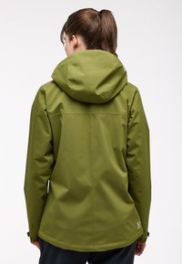 Grön vattentät jacka med en åtsittande huva, slät yta och en zip-försedd söm på baksidan. Reflekterande logotyp på nedre vänstra sidan.