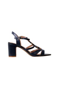 Sandale à talon en cuir noir avec bride à la cheville, accents décoratifs dorés et talon bloc sur fond blanc.