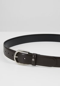 Cintura in pelle marrone con fibbia in metallo argento, caratterizzata da una superficie liscia e numerosi fori per la regolazione. Accentuata da dettagli di cucitura.