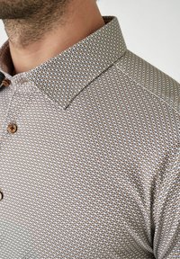 Bruine geblokte blouse met een knoopkraag. beschikt over een textuurstof met kleine cirkelvormige ontwerpen in afwisselende kleuren.