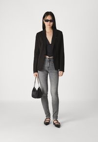 Blazer negro, top corto negro, jeans ajustados grises, bailarina negra puntiaguda. Sosteniendo un pequeño bolso negro con un asa de cadena.