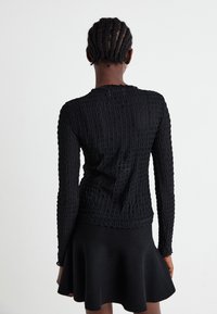 Svart langermet topp med en teksturert, rutenettlignende design. Stoffet er stripete, med en tettsittende silhuett og rund halskjæring.