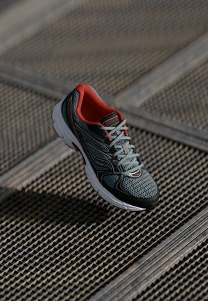 Grauer Sportschuh mit roten Akzenten, Obermaterial aus Netzgewebe und gepolsterter weißer Sohle, der komplexe Oberflächenstrukturen und ein schlankes Design aufweist.