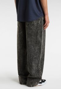 Baggy sorte denim jeans med en falmet tekstur, der har baglommer og en løs pasform, parret med sort og hvidt træningssko.