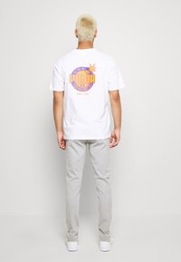 White short-sleeve t-shirt featuring a colorful "PUMA" graphic on the back, paired with light gray striped pants and white shoes.