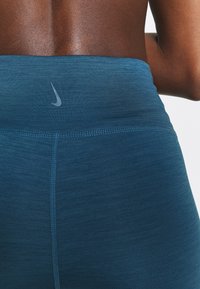Tummansininen korkeavyötäröinen leggingit, joissa on teksturoitu pinta, ohuella Nike-logolla vyötärössä ja litteillä saumoilla mukavuutta varten.