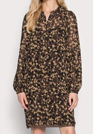 Femme portant une robe ample à manches longues, longueur genou, avec un motif tacheté marron et noir et un petit col en V.