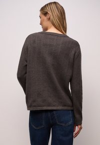 Dunkelgrauer Strickpullover mit lockerem Schnitt, überschnittenen Schultern und geripptem Kragen. Kombiniert mit blauen Denim-Jeans, Ansicht von hinten.