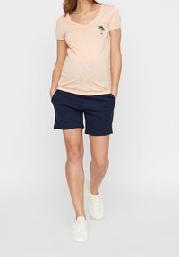 Peach short-sleeve shirt with palm tree embroidery, paired with navy shorts. The outfit features a relaxed fit and light fabric, complemented by white sneakers.