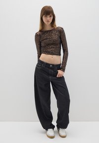 Crop top nero con paillettes a maniche lunghe abbinato a jeans scuri dal fit morbido. La modella indossa sneakers bianche con dettagli marroni.