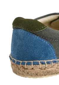 Parte superior de tela verde con detalles en gamuza azul, suela de yute y costuras en contraste. Diseño de slip-on de perfil bajo con tacón redondeado.