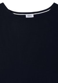 Encolure de chemise bleu marine avec une étiquette blanche affichant le nom de la marque Cecile cousue à l'intérieur du col.