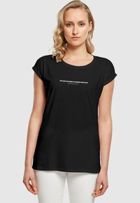 Sort bomuld t-shirt med oprullede ærmer og rund halsudskæring. Påtrykt tekst i hvid læser: "DU HAR MAGTEN TIL AT FORANDRE DIT LIV."