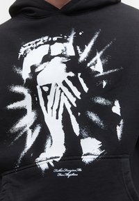Black hoodie with white abstract hand and face design radiating streaks, featuring small cursive text near the pocket.