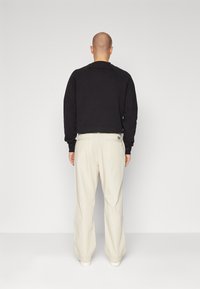 Svart hettegenser med rund hals og ribbestrikket mansjetter, kombinert med kremfargede vide bukser, synlig sømdetaljering og minimalistisk design.