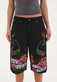 Pantalones cortos de mezclilla negra con gráficos florales coloridos y el texto "EL AMOR MUERE DIFICIL". Incluye bolsillos frontales y cierre de botón metálico.