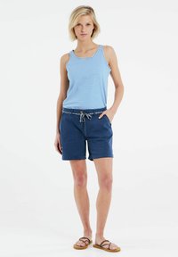 Canotta a righe blu e bianche, abbinata a pantaloni corti navy con coulisse e motivo floreale. Sandali con cinturini marroni completano il look.