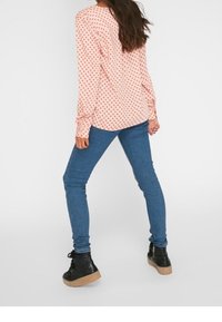 Camicia a maniche lunghe rosa con pois rossi, abbinata a jeans skinny blu e stivaletti neri con tacco alto.