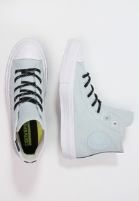 Jasnoniebieskie sneakersy typu high-top z białymi gumowymi czubkami i podeszwami. Czarne sznurowadła przetykane przez oczka, z naszywką z logo po boku.