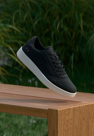 Sneaker in pelle nera con suola in gomma bianca, caratterizzata da un design strutturato, chiusura con lacci e sottili accenti rossi sul lato.