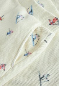 Weißes Strickgewebe mit einem strukturierten Muster und kleinen, bunten Vogelmotiven in Pink, Blau und Rot überall verteilt.