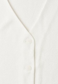 Gros plan sur un tissu de cardigan en maille blanche avec deux boutons blancs et un col en V.