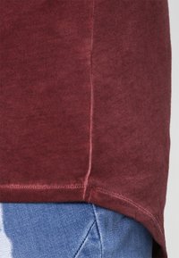 Burgundowa bawełniana koszulka z okrągłym dołem i subtelną teksturą, w połączeniu z jasnymi dżinsami, prezentująca swobodny look.