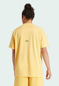 Żółta bawełniana koszulka z krótkim rękawem, okrągłym dekoltem i nadrukowanym logo na plecach. Gładka faktura i luźny krój.