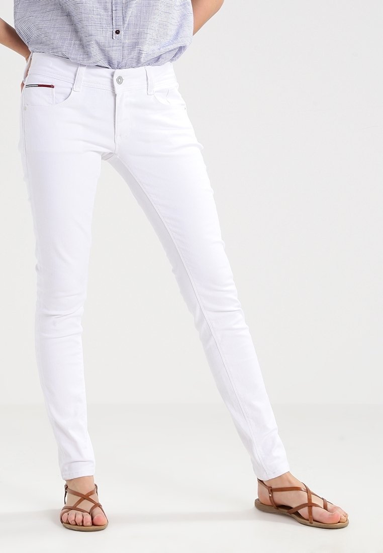 Jeans skinny blancos con una cintura de media altura, cierre con botón y diseño clásico de cinco bolsillos. Textura suave con un acento rojo en el bolsillo.