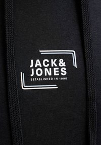 Tissu de sweat-shirt noir avec un logo imprimé blanc comprenant le texte "JACK & JONES" et "ESTABLISHED IN 1990", encadré par de fines lignes blanches.