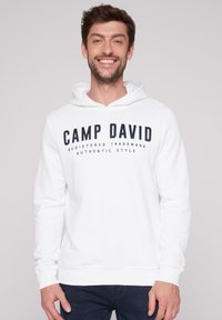 Witte hoodie met een voorzijde logo waarop "CAMP DAVID" in vetgedrukte marineblauwe letters is afgebeeld, gemaakt van zachte stof met lange mouwen en geribde boorden.