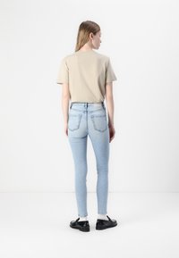 Camiseta beige de manga corta combinada con vaqueros ajustados de un azul claro. Los vaqueros tienen dos bolsillos traseros y una textura desgastada. Unos zapatos negros completan el look.