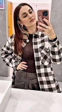 Black and white checkered button-up shirt with long sleeves, worn over a brown top and gray high-waisted trousers. Smooth fabric and pockets.