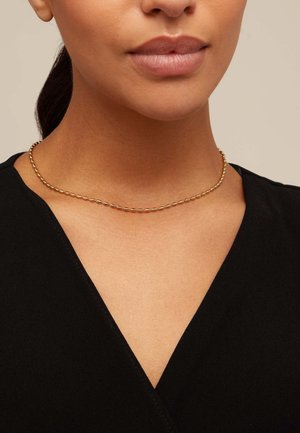Collar de cadena en tono dorado con eslabones redondeados y alargados. Lleva puesto alrededor del cuello, complementando una prenda negra con escote en V.