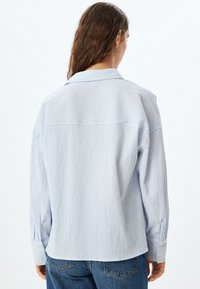 Camisa de rayas azul claro con un tejido texturizado, cuello clásico y mangas largas, con puños abotonados y un fit relajado.