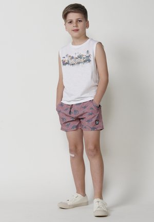 Bílé tílko s tropickým potiskem a šortky s červeným vzorem. Doplněno světlými teniskami, představujícími uvolněný letní outfit.