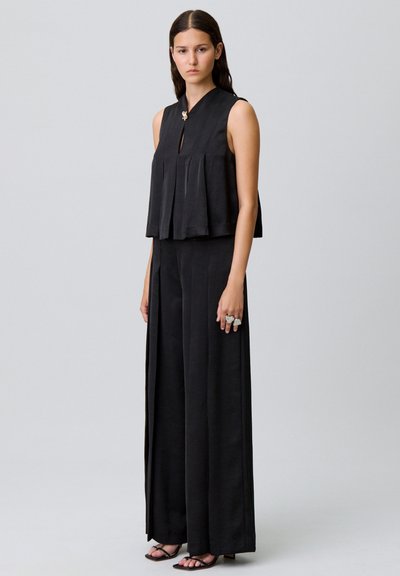 Top negro sin mangas con un diseño plisado y un detalle de ojal en el frente, combinado con pantalones de pierna ancha. Tejido suave y acentos de hardware mínimos.
