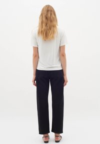 Tricou alb din bumbac cu mâneci scurte, asortat cu blugi negri cu talie înaltă și croi larg, și sandale negre cu bretele. Părul este lung și ondulat.