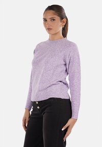 Maglione viola a maglia con scollatura rotonda, maniche lunghe e orlo leggermente aderente. Abbinato a pantaloni neri a vita alta con bottoni dorati.