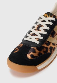 Sko med leopardprintet stof, sorte ruskinds-overlays, beige striber, hvide snørebånd og en gummisål på hvid baggrund.