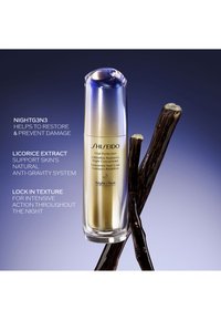 Klart glassflaske med gull- og sølvdetaljer, med avrundet topp. Mørke kvister plassert ved siden av flasken på en gradient blå bakgrunn.