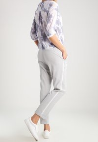 Pantalons fuselés gris clair avec des rayures blanches sur les côtés, associés à un chemisier lavande à motifs transparent et des baskets blanches.