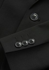 Giacca di tessuto nero in primo piano con una texture liscia, tre bottoni neri opachi con quattro fori e rever strutturati.