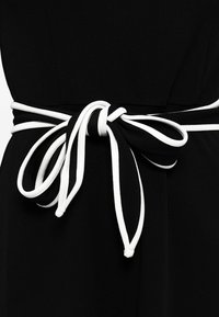 Ceinture en tissu noir nouée en nœud avec un détail de passepoil blanc autour de la taille d'un vêtement noir.