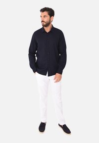 Camicia a maniche lunghe blu navy, slim fit, abbinata a pantaloni bianchi e scarpe nere. Design semplice, texture liscia e colore uniforme.