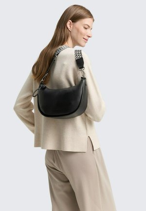 Schwarze Leder-Schultertasche mit runder Form, ausgestattet mit einem strukturierten Riemen und silbernen Hardware-Details. Trägt eine beigen Pullover.