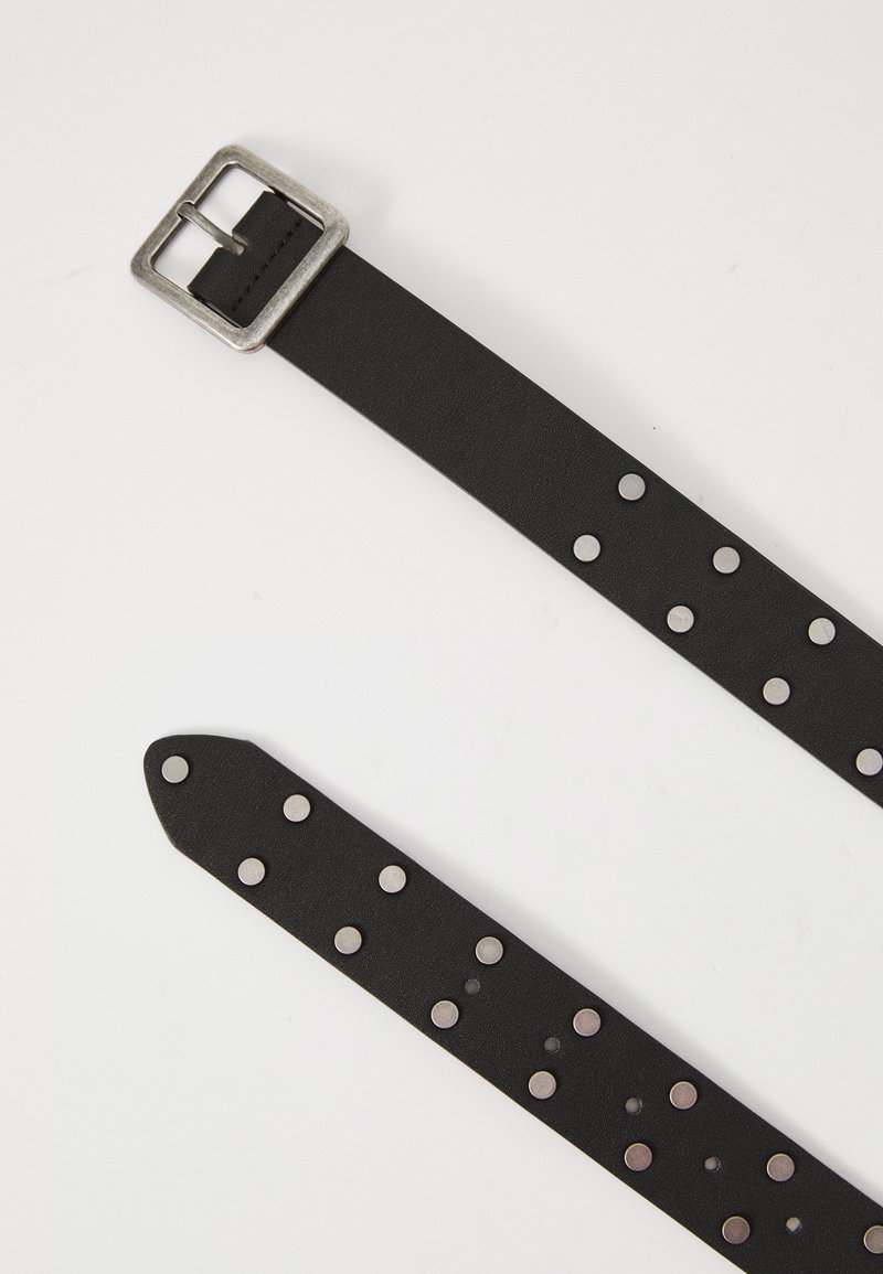 Cinturón de cuero negro con una hebilla cuadrada de plata, que presenta tachuelas metálicas circulares espaciadas uniformemente a lo largo de la correa para un detalle adicional.