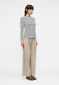 Μακρυμάνικη ριγέ μπλούζα σε μαύρο και άσπρο, συνδυασμένη με φαρδιά μπεζ παντελόνια. Καφέ μποτάκια με τακούνι συμπληρώνουν το σύνολο.