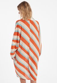 Robe ample de couleur orange, crème et bleu clair, avec de larges rayures diagonales, des manches longues et un col.